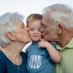Grandma and grandpa smooch the face of their 2 year old great grandson