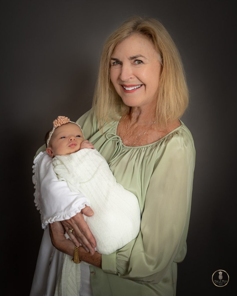 A grandmother poses holding her first grandchild in a portrait made by Brisson Imagery