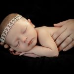 Newborn baby girl in her mothers hands wearing a diamond headband. Portrait by Brisson Imagery