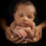Newborn baby boy posed in his mothers hands with his hands under her chin portrait by Brisson imagery