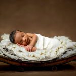 Newborn Baby boy laying on a bed of cream colored blankets sleeping. Portrait by Brisson Imagery