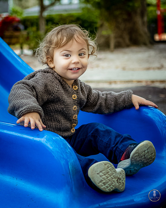 Toddler boy smiling big at the end of a blue slide