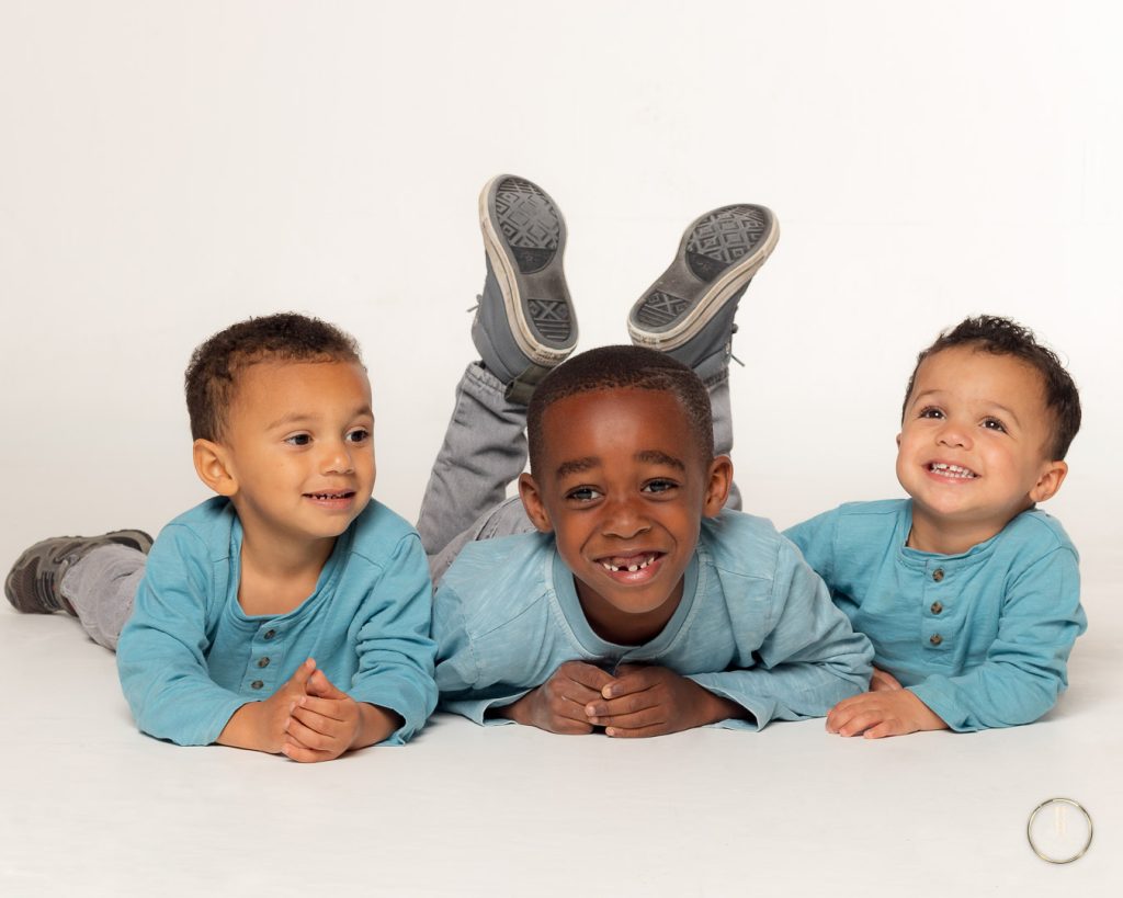 3 little boys lay on the ground on their tummies. feet over their heads. giggling. Portrait by Brisson Imagery