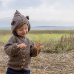 little boy in a bear sweater plays with marsh grass