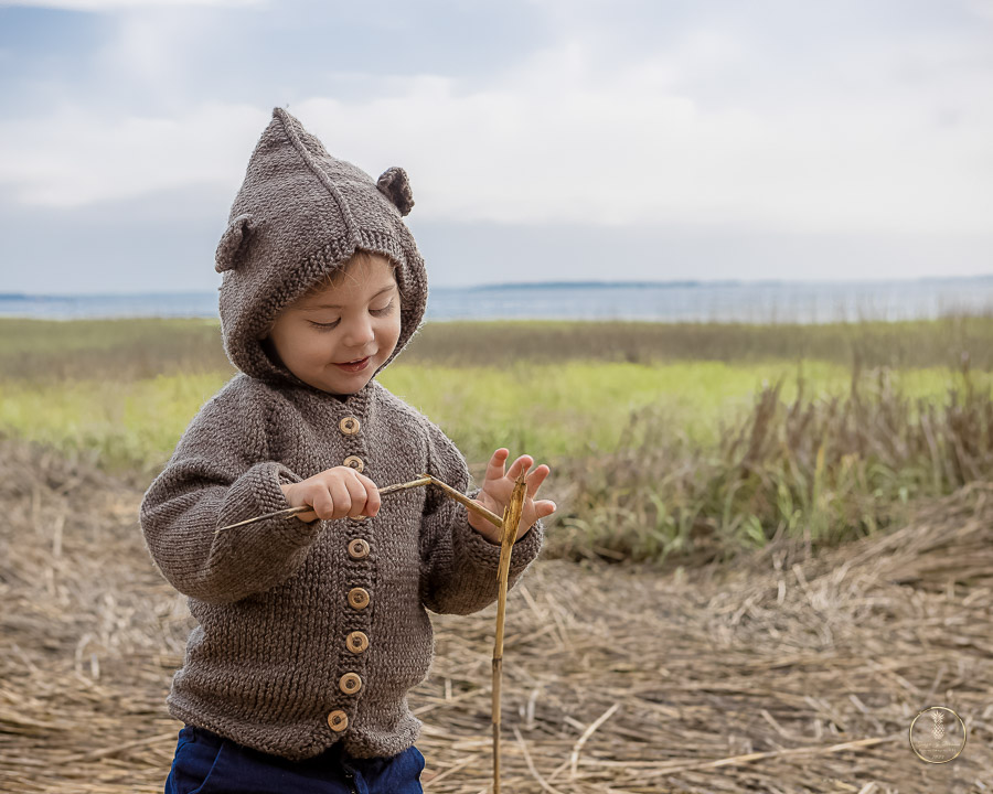 little boy in a bear sweater plays with marsh grass