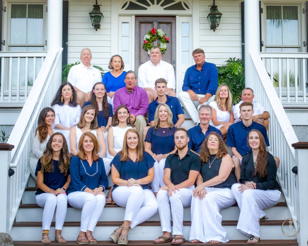 Large family portrait. 27 people sit on the front steps to a beach house.