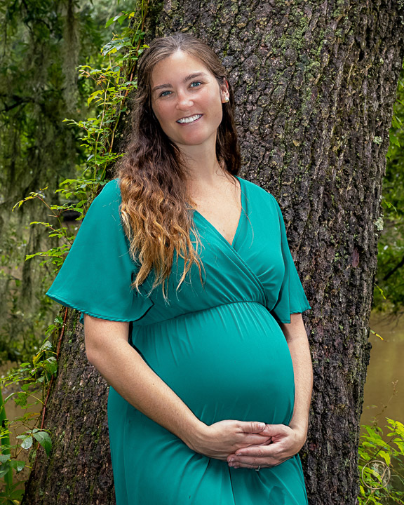 Maternity Portrait of a woman in green standing next to a creek. Portrait by Brisson Imagery
