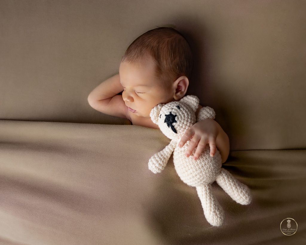 Newborn baby posed tucked in bed with a teddy bear. Portrait by Brisson Imagery