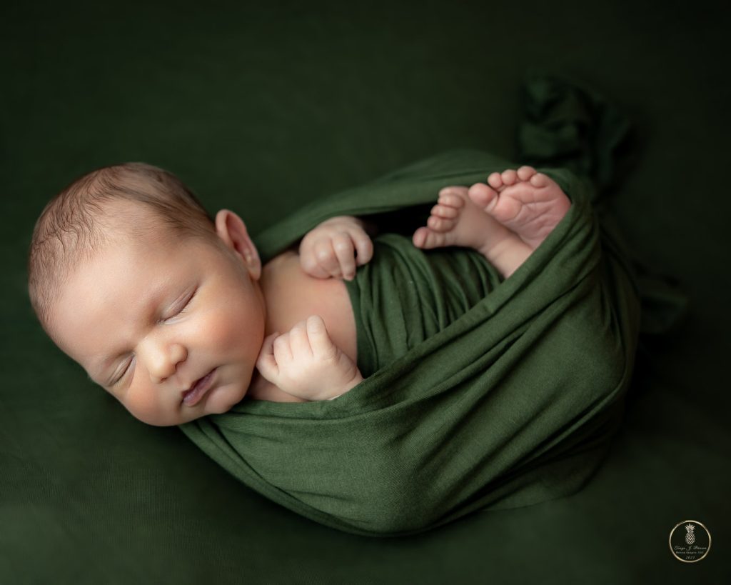 Newborn baby boy in green in the huck fin pose portrait by Brisson Imagery