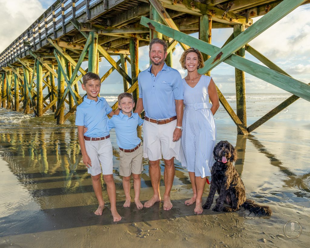 Family of 4 stand under the IOP pier with their dog in a family portrait by Brisson Imagery