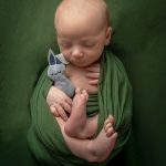 Newborn in green wrapped in the womb pose, holding a tiny stuffed bunny