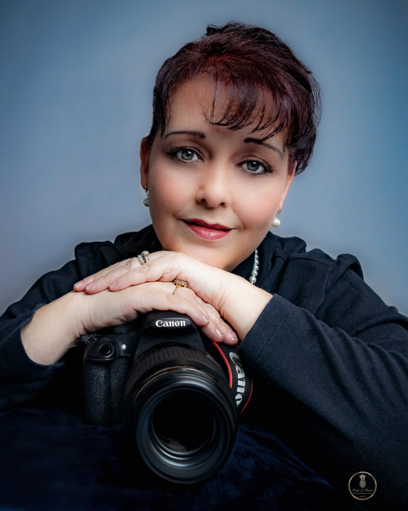 Self Portrait of Charleston Family Photograher, Tonya Brisson. She is wearing black and a pearl necklace and earrings. The is resting her chin on her hands, on top of her Canon EOS R camera.