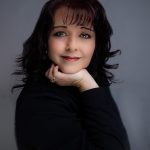Professional Photographer Tonya Brisson. Self Portrait. Gray backdrop, black shirt, long curly hair.