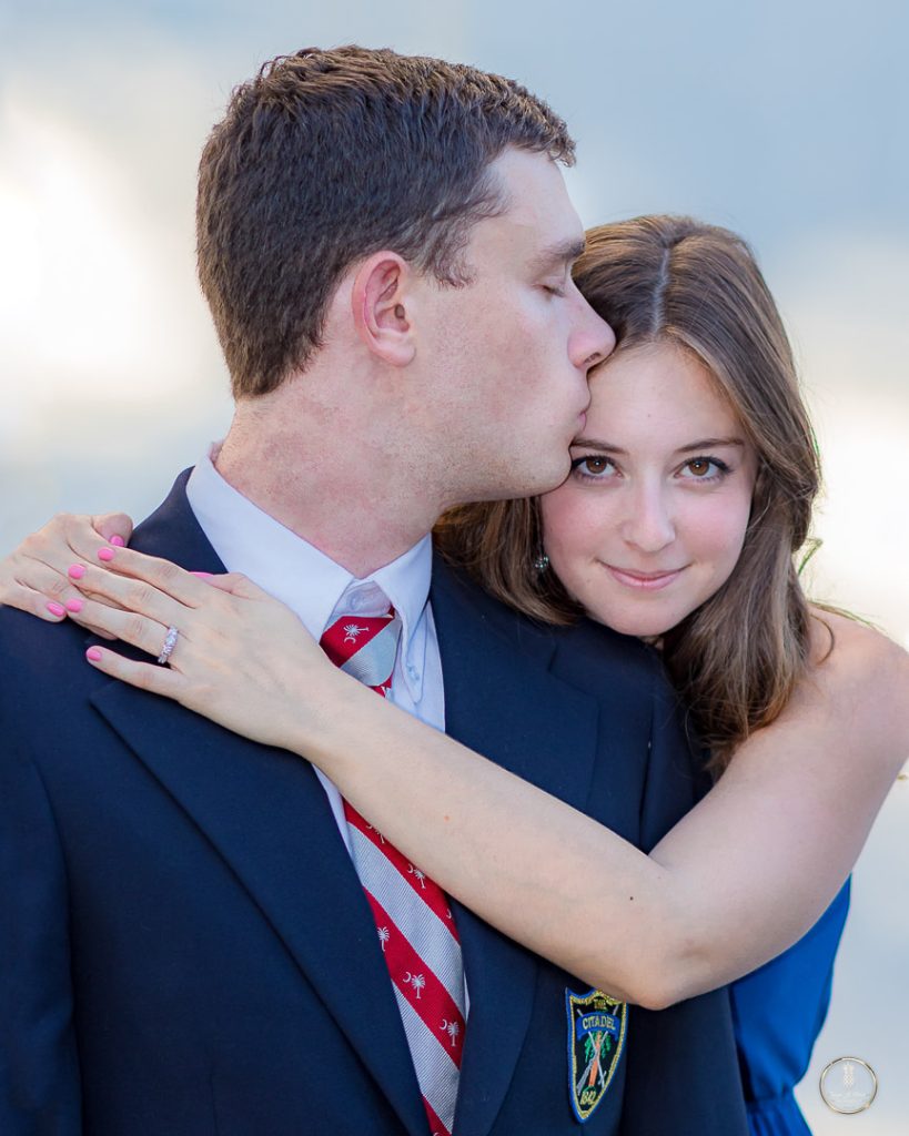 Engagement portrait by Brisson Imagery. Citadel Cadet kisses fiance on the temple whie she hugs his neck smiling at the camera. her engagement ring prominent to the camera