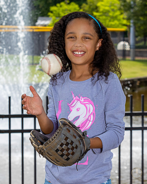 little girl tossing a baseball up in the air and catching it in her baseball glove