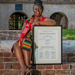College of Charleston Senior girl sits on steps displaying her framed degree in English
