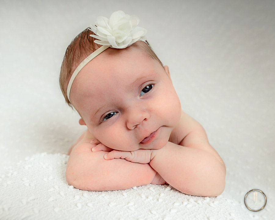 Charleston Newborn Photographer image of a baby girl doing the chin on hands pose with eyes open and smiling 
