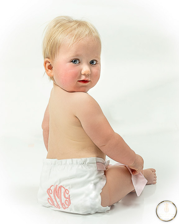 Baby girl with monogramed diaper cover looks over her shoulder at the camera