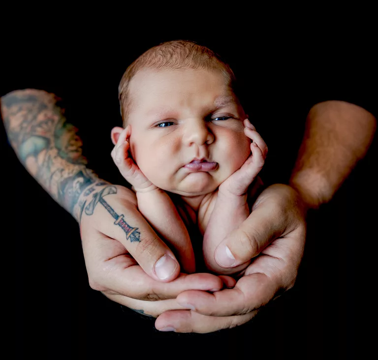 Newborn posed in fathers hands father has tatoos